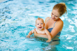 Mother and baby in pool, mother holding the baby and smiling