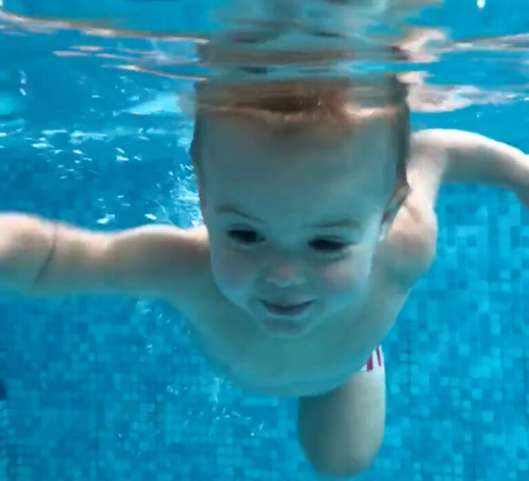 Baby swimming at swim lessons, holding breathe under water